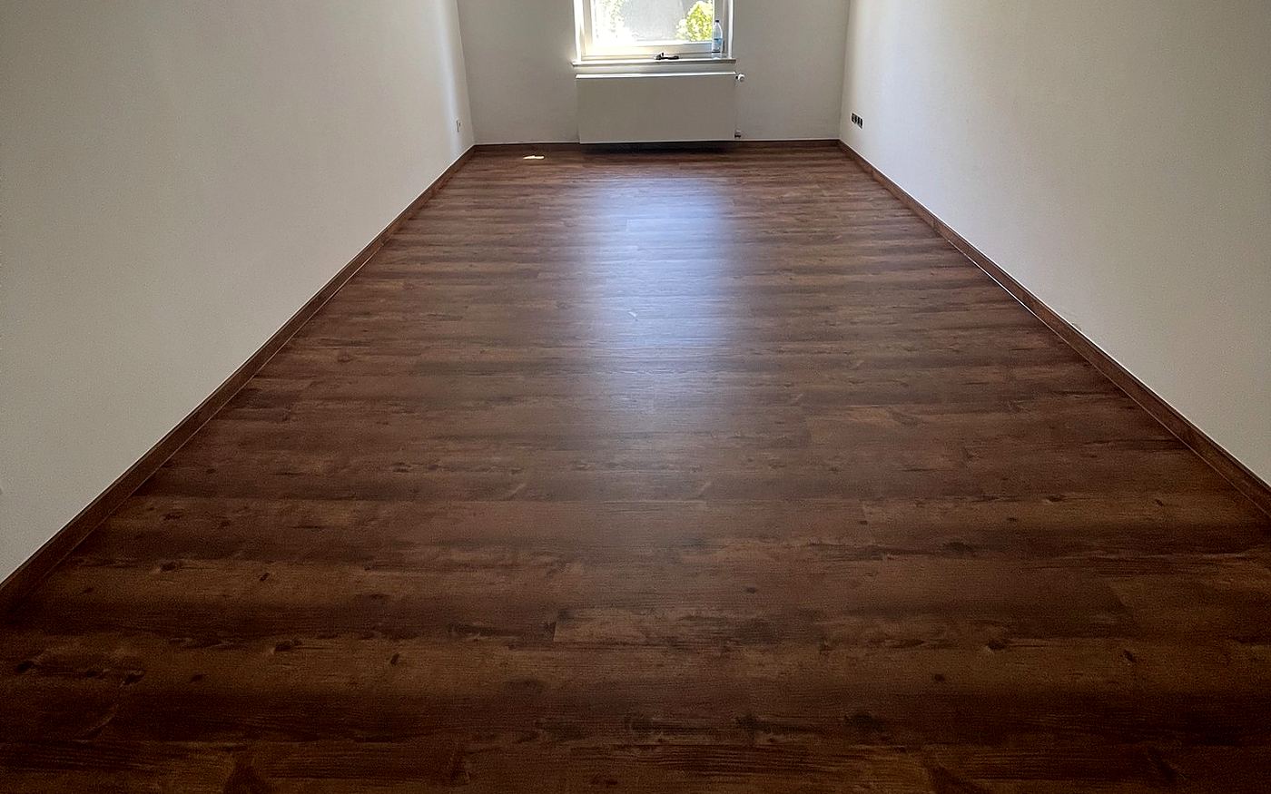 Frisch verlegtes Laminat in dunkler Dielenoptik in einem hellen leeren Raum in München
