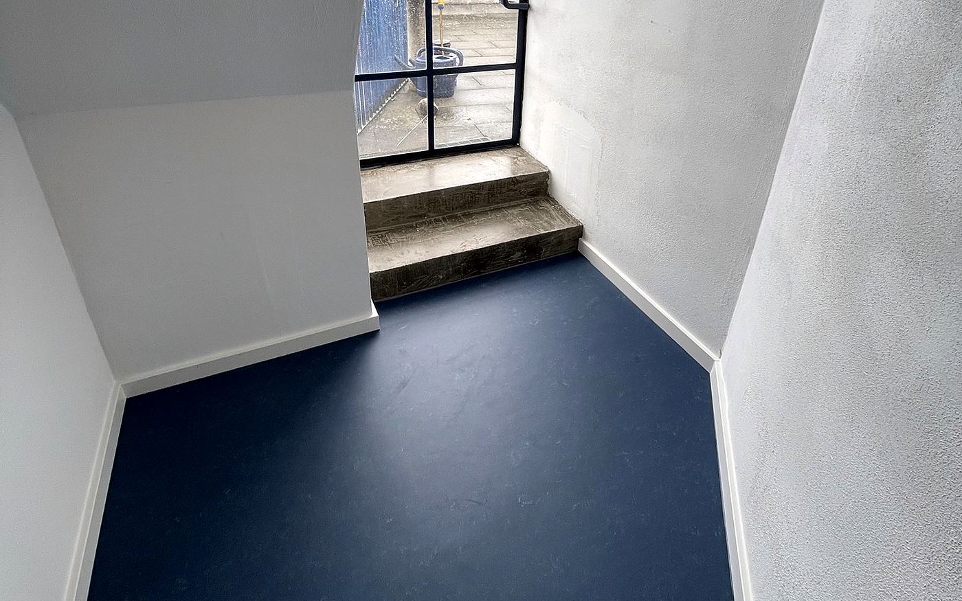 Flur mit dunkelblauem Linoleum und angrenzendem Treppenaufgang