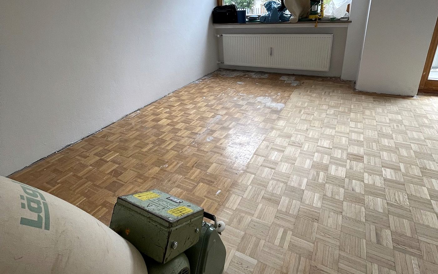 Mosaikparkett im Würfelmuster während des Schleifvorgangs mit Maschine im Raum