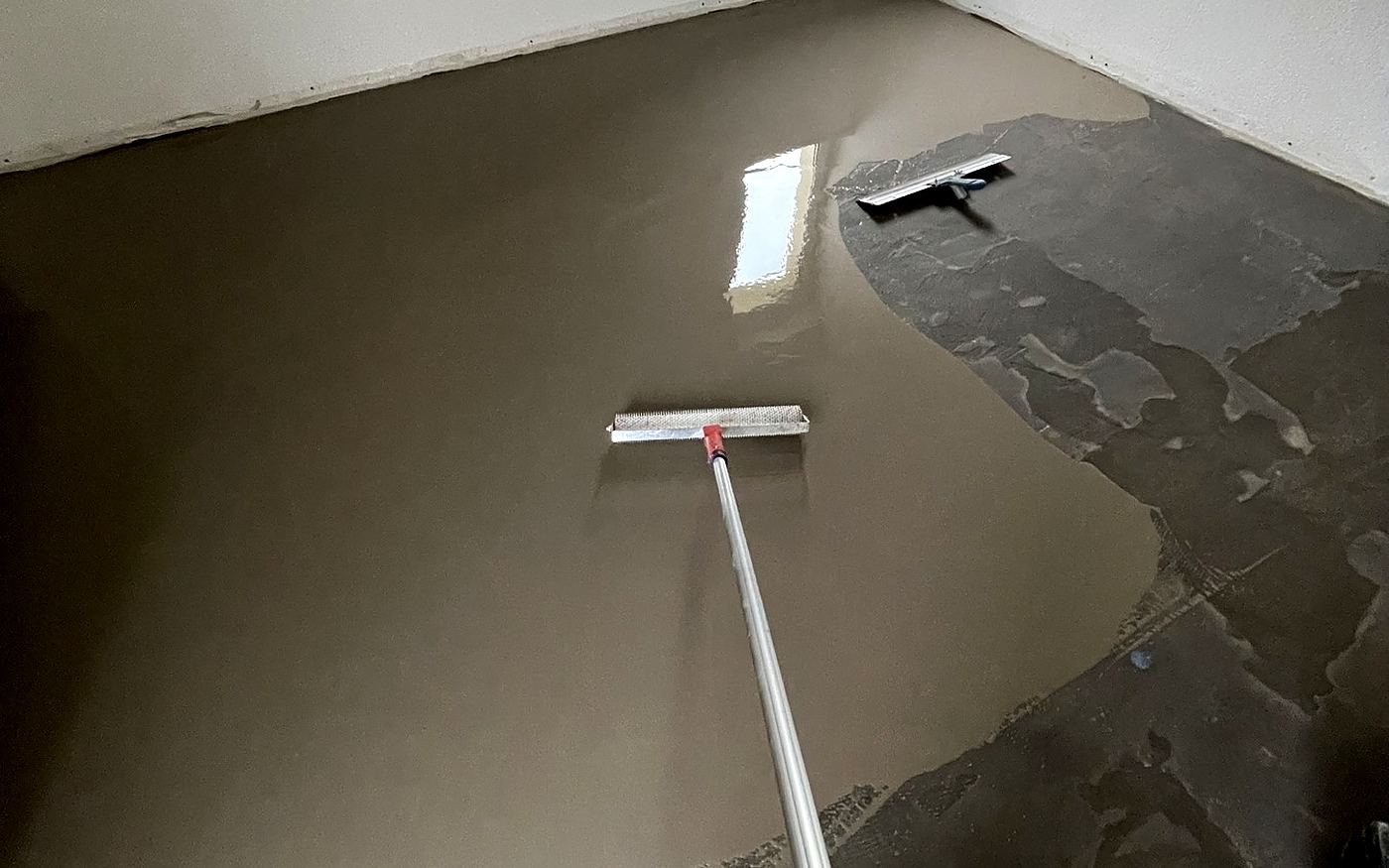 Ausgleichsmasse wird mit einer Rakel auf dem grundierten Untergrund verteilt